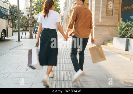 Abbassare la sezione corpo di un giovane turista giovane a piedi da store windows e tenendo la carta shopping bags in una città di destinazione. Foto Stock