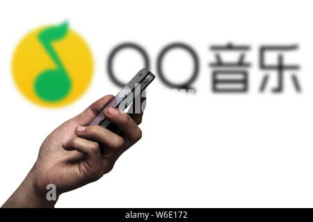 --FILE -- un telefono cellulare utente guarda il suo smartphone accanto a un logo di QQ Musica di Tencent in Ji'nan city, est della Cina di provincia di Shandong, 16 Settembre Foto Stock