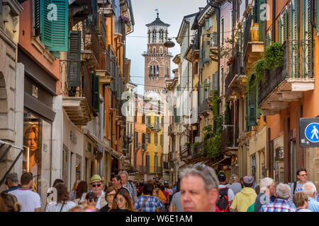 A Verona, Italia, i turisti affollano il design elegante e colorato, area pedonale Via Giuseppe Mazzini. Il XII secolo Torre dei Lamberti sorge al di là. Foto Stock