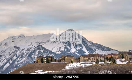 Telaio Panorama case con vista del torreggiante picco neve montagna e cielo nuvoloso in inverno Foto Stock