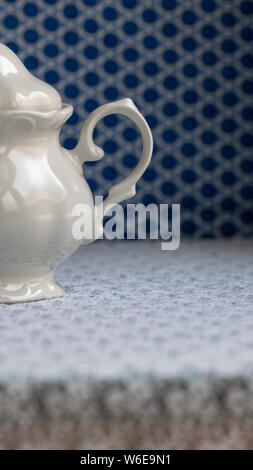 Zucchero bianco ciotola su una bianca tovaglia di pizzo. Blu non focalizzato sullo sfondo geometrico. Foto Stock