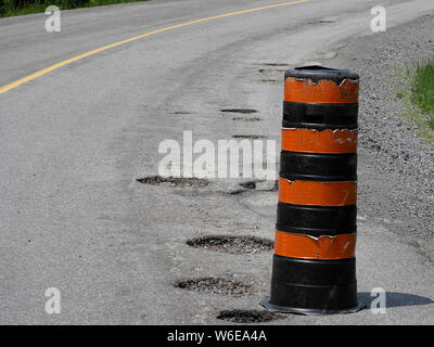 Un arancione e nero cono di traffico segnando una serie di profonde buche lungo una curva sulla strada. Foto Stock