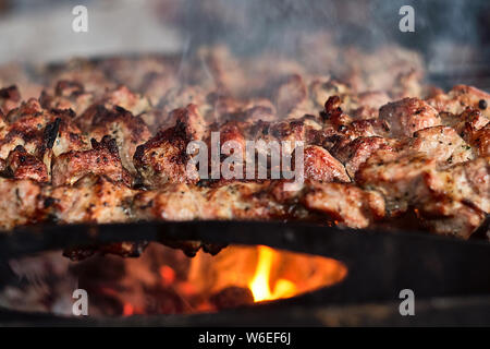 Tradizionale barbecue caucasica spiedini di carne alla griglia su bastoni di essere cotta sul fuoco aperto con fumo, vista ravvicinata. Foto Stock