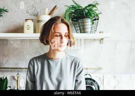 Giovane donna in abito grigio sulla cucina, interni Scandinavo, vita lenta Foto Stock