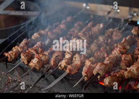 Tradizionale barbecue caucasica spiedini di carne alla griglia su bastoni di essere cotta sul fuoco aperto con fumo, vista ravvicinata. Foto Stock
