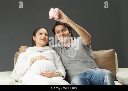 Coppia che guarda la banca piggy e sorridente Foto Stock