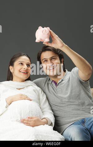 Coppia che guarda la banca piggy e sorridente Foto Stock