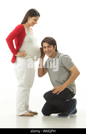 Uomo che ascolta lo stomaco della donna incinta Foto Stock