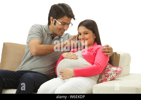 Donna incinta che parla sul telefono cellulare con il marito che tiene esso Foto Stock