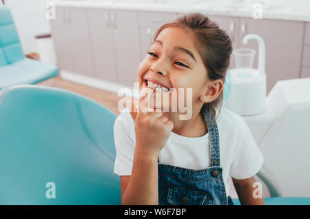 Razza mista poco paziente mostrando il suo perfetto sorriso toothy seduti dentisti sedia Foto Stock