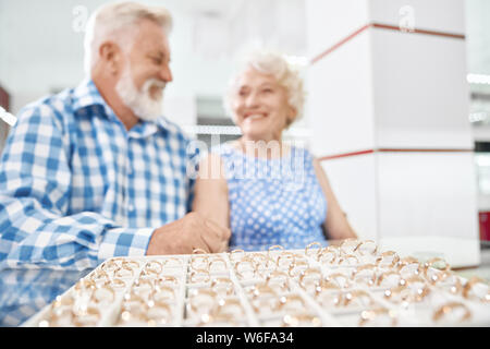 Allegro di età matura in abbigliamento elegante seduti a tavola in negozio Gioielli e piacevolmente sorpresi della bella collezione di anelli in oro. Concetto di customer service e l'acquisto. Foto Stock