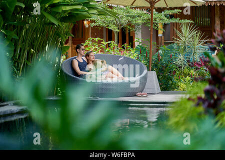 Candid shot della giovane coppia caucasica lounging nella sedia moderna nei pressi di lussuosa piscina di tropical hotel e spa a Bali Foto Stock