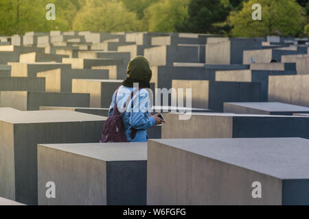 Berlino, Germania - 26 settembre 2018: Donna cammina attraverso i blocchi del Monumento all'assassinato ebrei d'Europa, con una prospettiva di profondità e verde Foto Stock