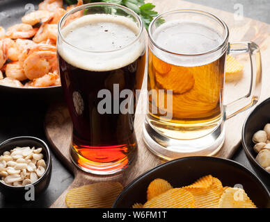 Progetto di birra e spuntini su sfondo di pietra. Dadi, patatine fritte, salsicce e gamberetti Foto Stock