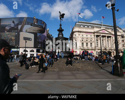 Turisti che si godono il sole sui passi che circonda il Shaftesbury Memorial fontana e di Piccadilly Circus a Londra in un giorno caldo in marzo. Foto Stock