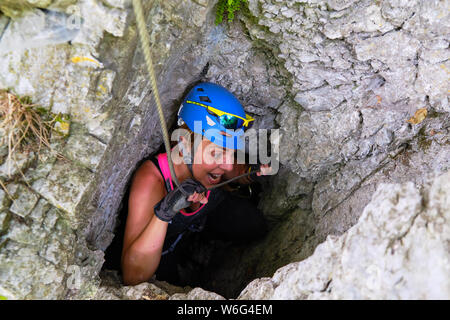 Scalatore ragazza ingannare intorno a via ferrata, mimando mordere il cavo, mentre esce da una grotta attraverso una stretta apertura, su un percorso difficile Foto Stock
