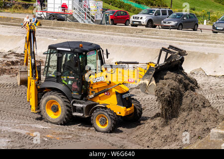 JCB Back Hoe la pulizia di una spiaggia. Foto Stock