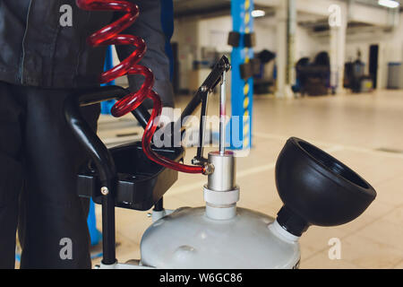 Cambio dell'olio nel cambio automatico. Riempire l'olio attraverso il tubo. Auto stazione di manutenzione. Rosso dell'olio per ingranaggi. Le mani del meccanico di automobili in olio. Foto Stock