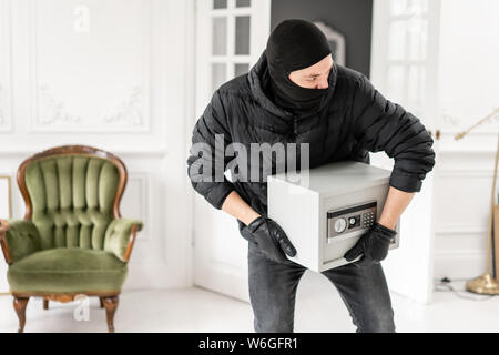 Ladro con nero balaclava rubare moderno cassetta di sicurezza elettronica. Il ladro commette un reato in un appartamento di lusso con stucco. Foto Stock