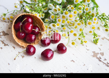 Waffle cup con ciliegie contro il vecchio tavolo in legno, bouquet di margherite sullo sfondo, close-up Foto Stock