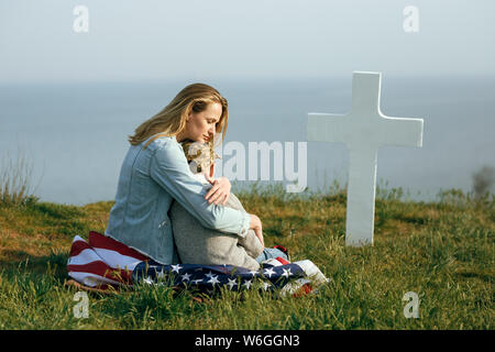 Madre e figlio sono seduti sulla tomba di un soldato. La mamma ha portato il suo figlio per la tomba di suo padre il memorial day 27 maggio Foto Stock