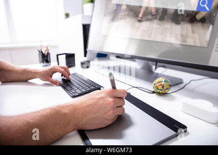 Designer che lavora sulla tavoletta digitale utilizzando la penna stylus su bianco Desk al luogo di lavoro Foto Stock