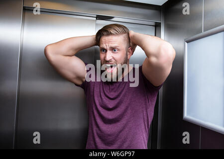 L uomo che soffre di claustrofobia intrappolato all'interno di ascensore urlando Foto Stock