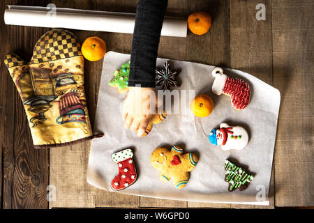 Vista dall'alto su come un bambino prende una vetrata di panpepato di Natale figurina da un tavolo di legno. Foto Stock