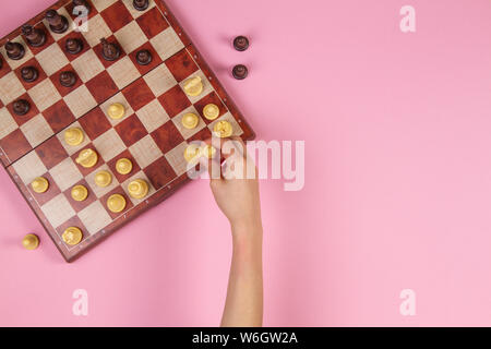 Il capretto con le mani su una scacchiera giocare a scacchi gioco su sfondo rosa, vista dall'alto Foto Stock