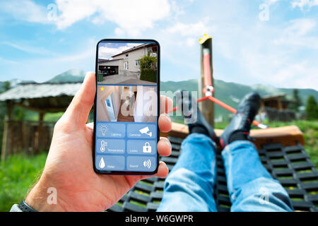 Uomo disteso in amaca a guardare video TVCC da casa sistema di sicurezza Foto Stock