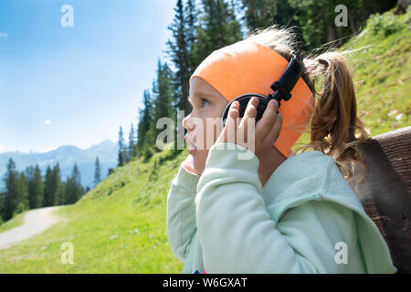 Bambina con le cuffie ascoltando musica in montagna Foto Stock