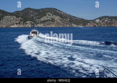 Imbarcazione a motore accelerando rendendo le onde spumeggianti in blu mediterraneo acqua su una soleggiata giornata estiva a Mallorca, Spagna. Foto Stock