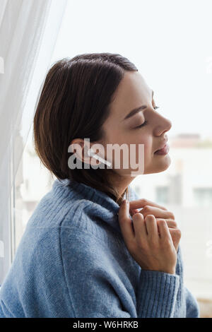 Ragazza in un maglione blu dalla finestra con le cuffie Foto Stock