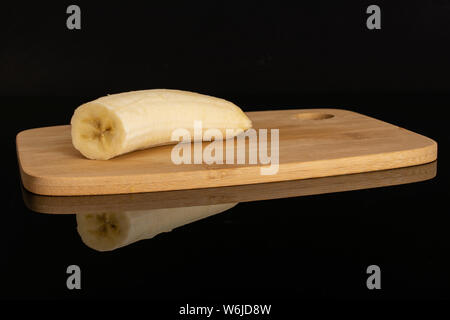 Sbucciate una metà di ripe banana giallo sul bambù tagliere isolato sul vetro nero Foto Stock