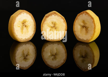 Gruppo di tre fette di ripe banana giallo nella riga isolata sul vetro nero Foto Stock