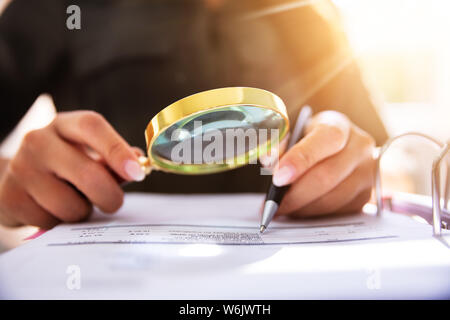 Close-up di un imprenditore la mano che tiene la lente di ingrandimento su fattura al posto di lavoro Foto Stock