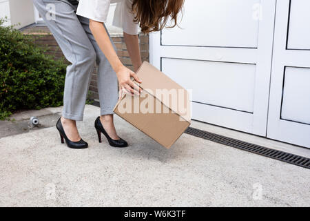 Sorridente giovane donna spiata fino il pacco consegnato presso la porta d'ingresso Foto Stock