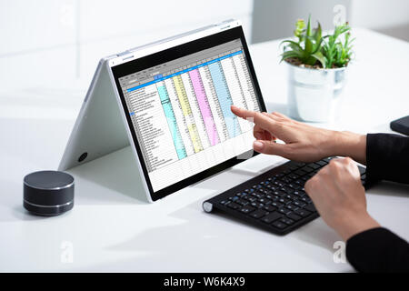 Close-up di una imprenditrice la mano esaminando un foglio di calcolo sul computer portatile in ufficio Foto Stock