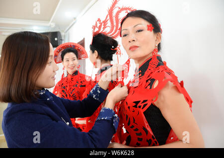 36-anno-vecchio artigiano cinese Liang Ying, un ereditiere di carta-talee, aiutare i modelli testa di usura Accessori, mantelli e orecchini in per il taglio della carta Foto Stock