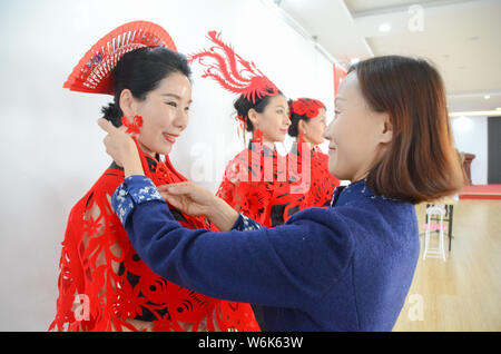 36-anno-vecchio artigiano cinese Liang Ying, un ereditiere di carta-talee, aiutare i modelli testa di usura Accessori, mantelli e orecchini in per il taglio della carta Foto Stock