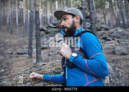 Ritratto di runner atleta con la barba di bere acqua dal tubo di hydropack nella foresta Foto Stock