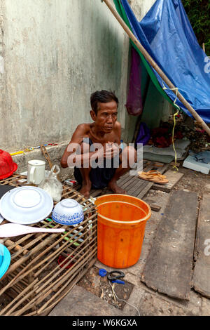 Un anziano senzatetto cambogiano si siede vicino alla sua casa sgangherato su una strada di città in Kampong Cham, Cambogia. Foto Stock