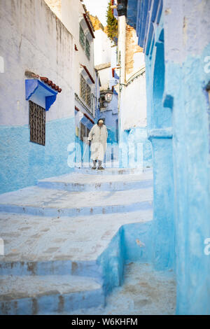 Un marocchino uomo vecchio, indossando il tradizionale Djellabah è a piedi attraverso il stretto vicoletto di Chefchaouen, Marocco. Foto Stock