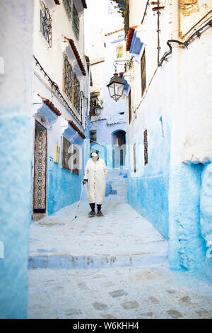 Un marocchino uomo vecchio, indossando il tradizionale Djellabah è a piedi attraverso il stretto vicoletto di Chefchaouen, Marocco. Foto Stock