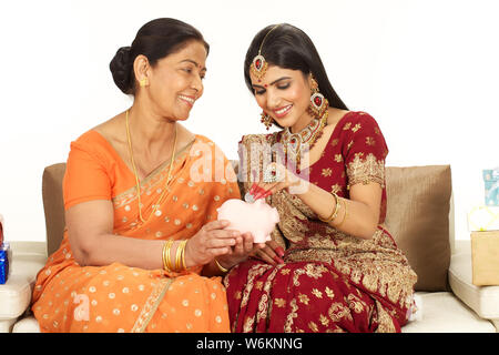 Woman putting coin into a piggy bank with her mother Stock Photo