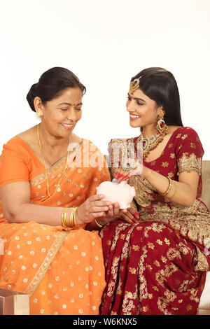 Woman putting coin into a piggy bank with her mother Stock Photo