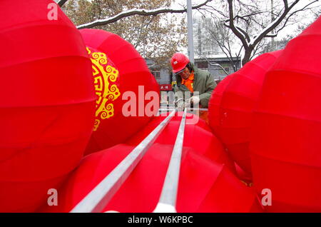 Un lavoratore cinese riaggancia lanterne rosse per celebrare la prossima festa della primavera o il nuovo anno cinese (anno del cane) su una strada a Xi'an City, Foto Stock