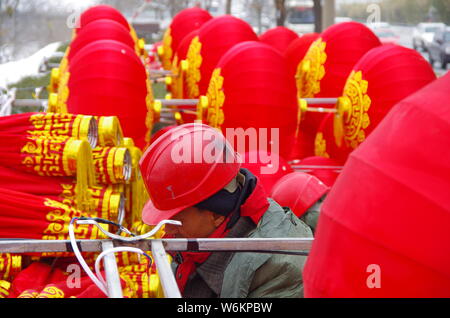 Un lavoratore cinese riaggancia lanterne rosse per celebrare la prossima festa della primavera o il nuovo anno cinese (anno del cane) su una strada a Xi'an City, Foto Stock