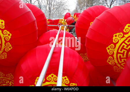 Un lavoratore cinese riaggancia lanterne rosse per celebrare la prossima festa della primavera o il nuovo anno cinese (anno del cane) su una strada a Xi'an City, Foto Stock