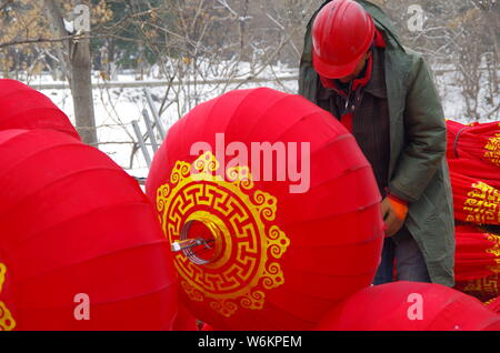 Un lavoratore cinese riaggancia lanterne rosse per celebrare la prossima festa della primavera o il nuovo anno cinese (anno del cane) su una strada a Xi'an City, Foto Stock